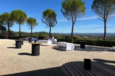 Chaises blanches alignées en extérieur face à une arche décorée, avec vue sur un paysage vallonné et des arbres.
