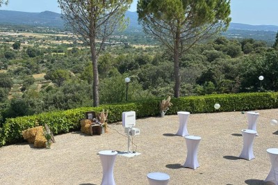 Chaises blanches alignées en extérieur face à une arche décorée, avec vue sur un paysage vallonné et des arbres.