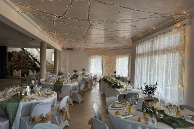 Chaises blanches alignées en extérieur face à une arche décorée, avec vue sur un paysage vallonné et des arbres.