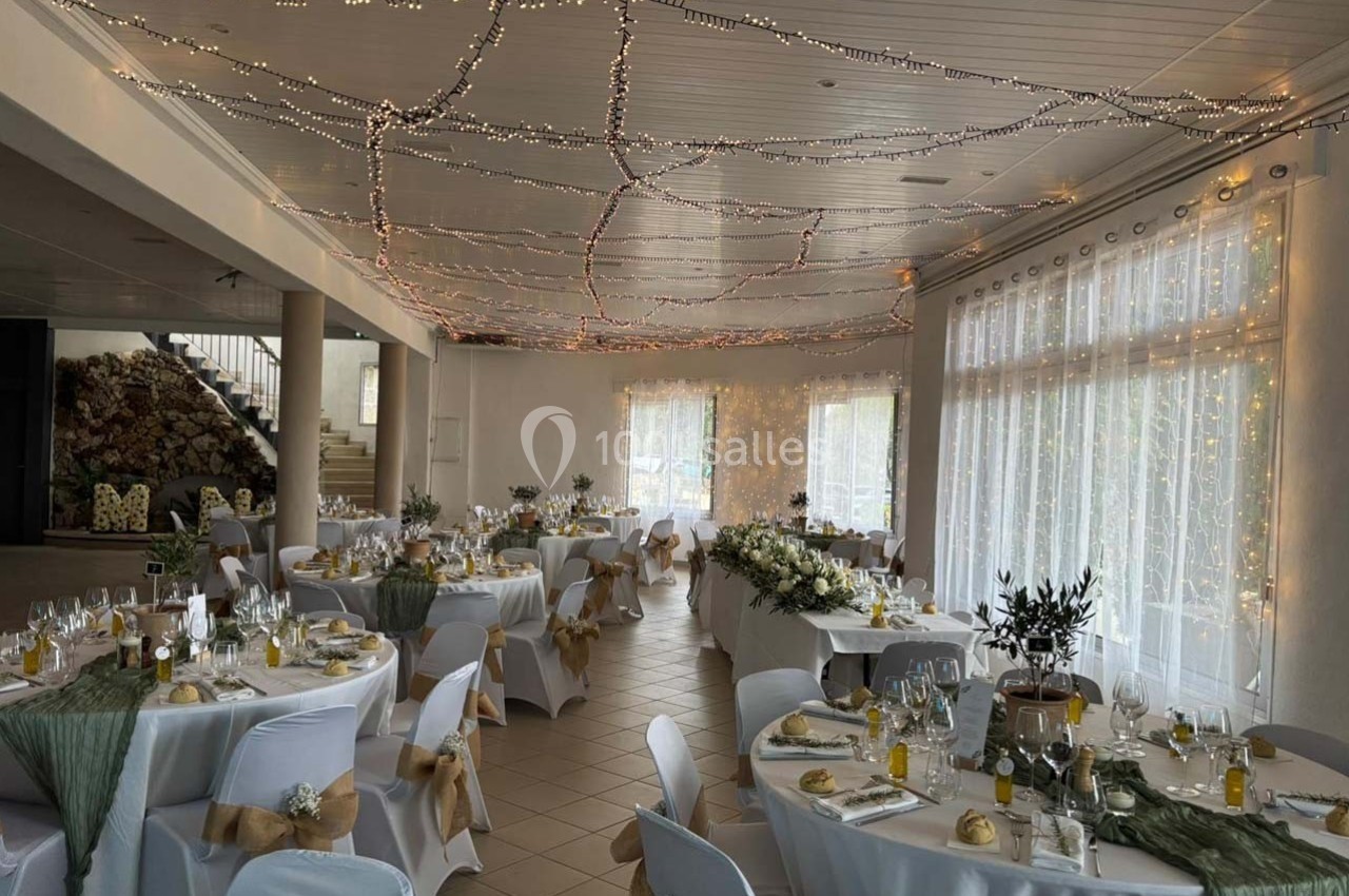 Salle de réception décorée pour un événement, avec tables dressées, nappes blanches et guirlandes lumineuses au plafond.