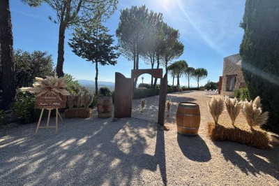 Chaises blanches alignées en extérieur face à une arche décorée, avec vue sur un paysage vallonné et des arbres.