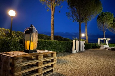 Chaises blanches alignées en extérieur face à une arche décorée, avec vue sur un paysage vallonné et des arbres.
