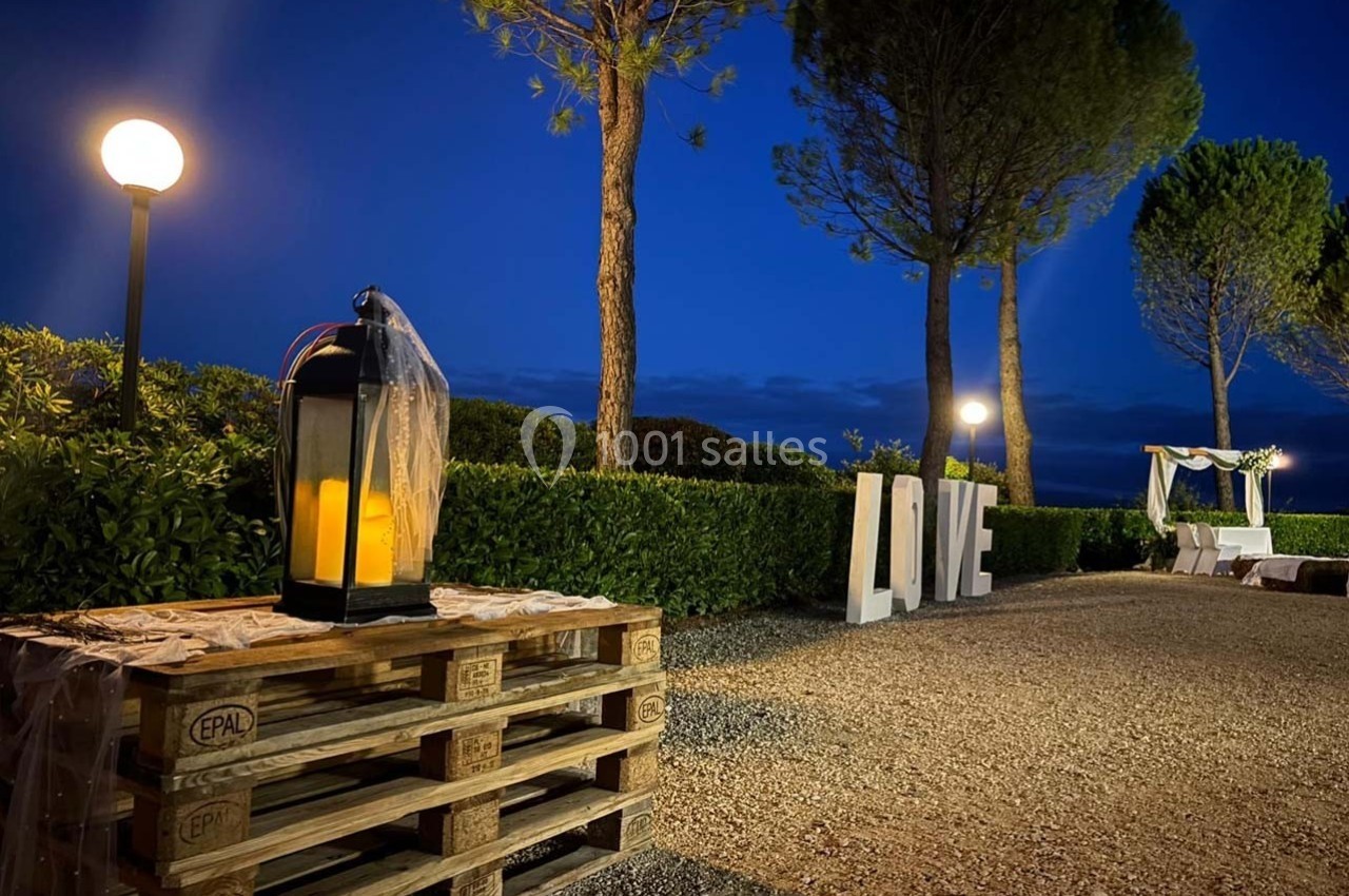 Lanternes allumées sur des palettes en bois, décor extérieur nocturne avec arbres, buissons et lettres ’LOVE’.