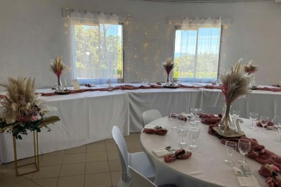 Chaises blanches alignées en extérieur face à une arche décorée, avec vue sur un paysage vallonné et des arbres.