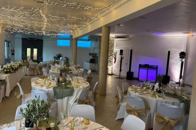Chaises blanches alignées en extérieur face à une arche décorée, avec vue sur un paysage vallonné et des arbres.