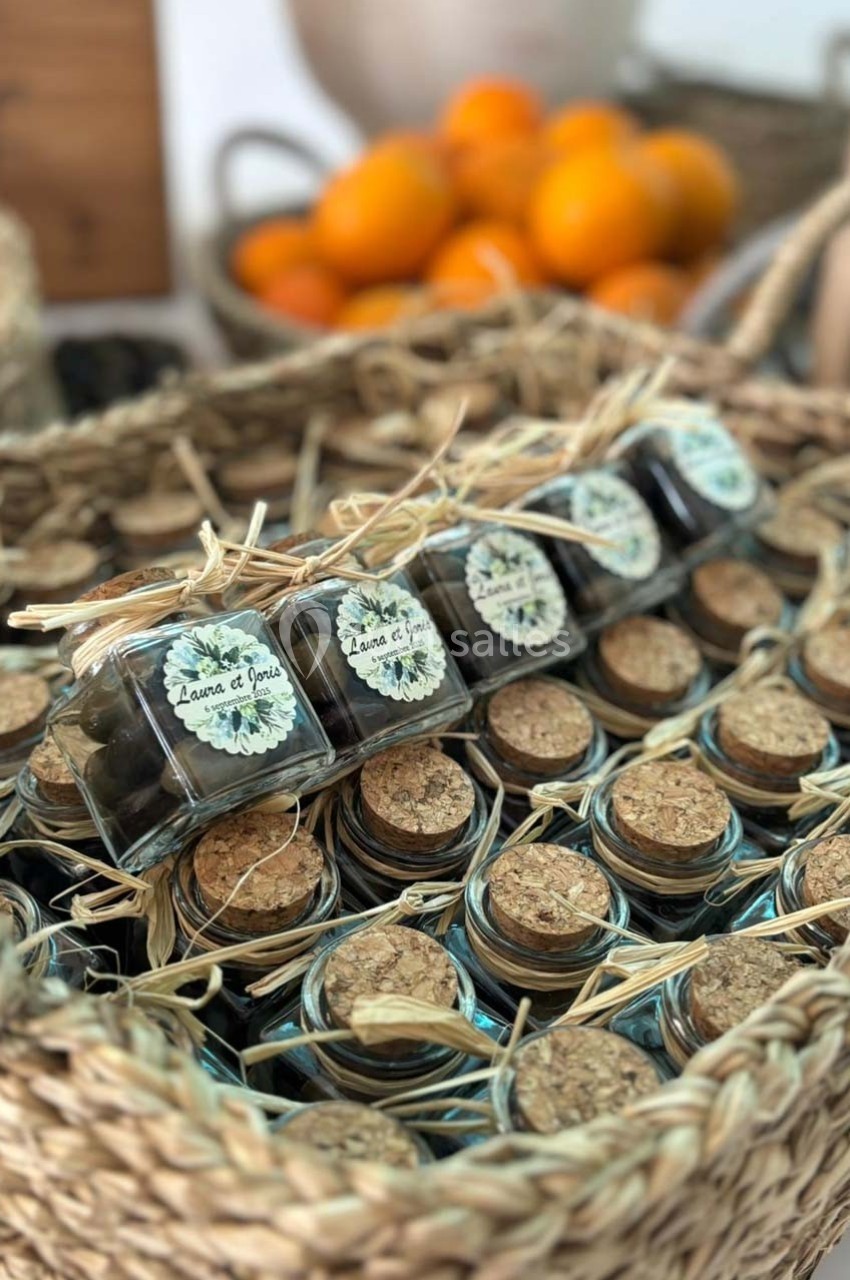 Petits pots en verre avec bouchons en liège, disposés dans un panier en osier, avec des oranges en arrière-plan.