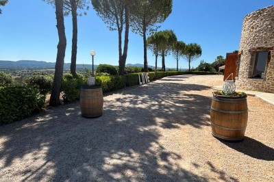 Chaises blanches alignées en extérieur face à une arche décorée, avec vue sur un paysage vallonné et des arbres.