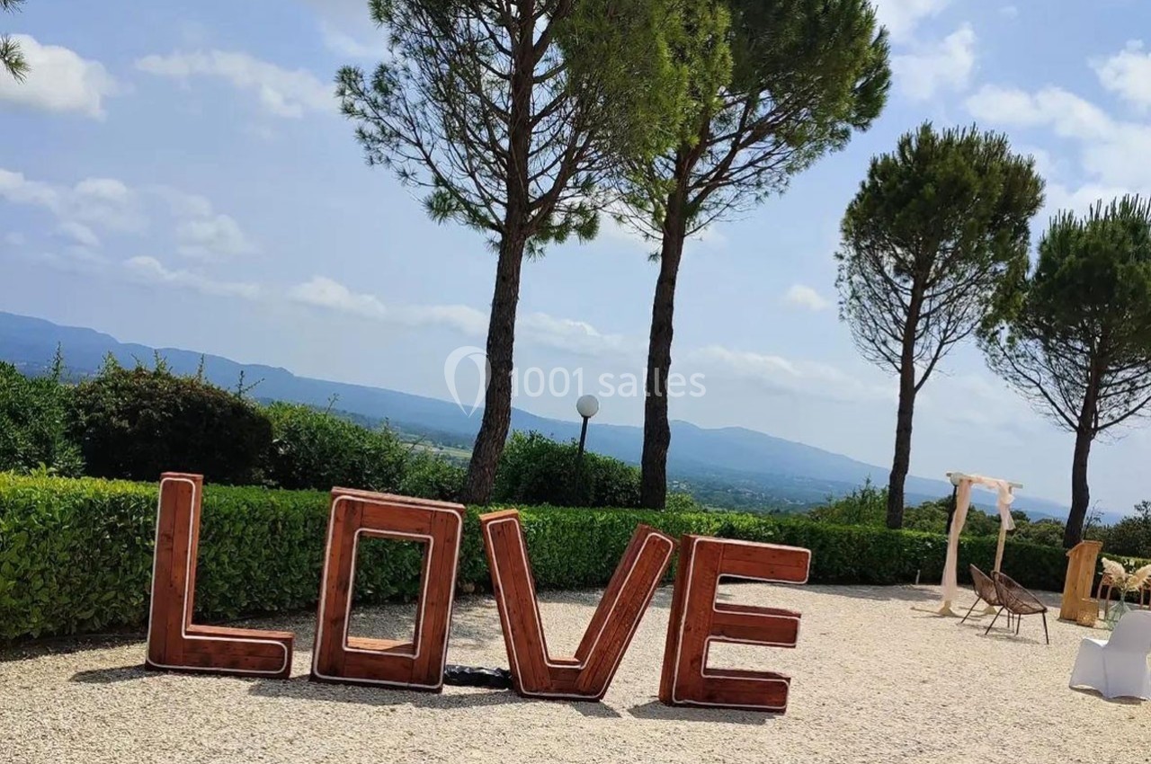 Lettres géantes formant le mot ’LOVE’ dans un jardin avec des arbres, des montagnes en arrière-plan et un ciel dégagé.