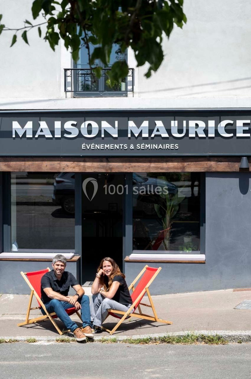 Deux personnes assises sur des chaises longues devant un bâtiment nommé ’Maison Maurice, Événements & Séminaires’.