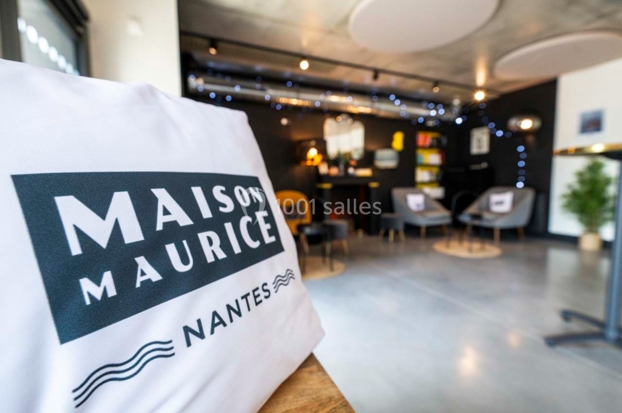 Vue d'un espace intérieur moderne avec un coussin marqué ’Maison Maurice Nantes’ au premier plan.