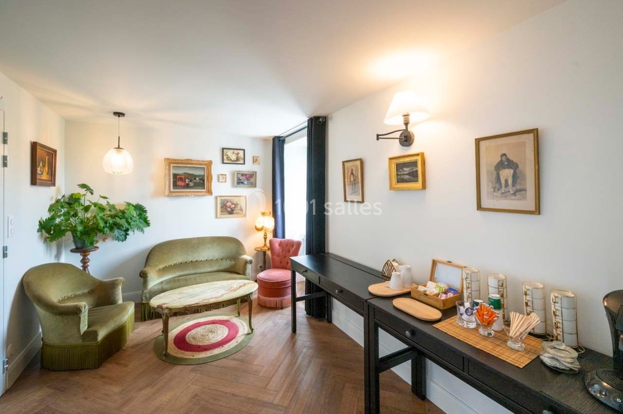 Salon lumineux avec canapé, fauteuils, table basse, décorations murales et coin avec boissons et collations sur une console.