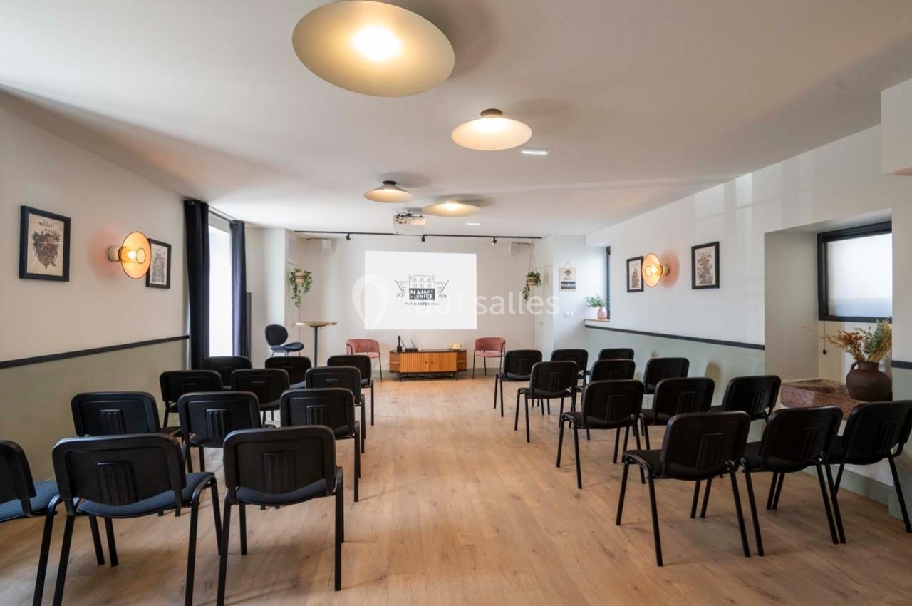 Salle lumineuse aménagée avec des rangées de chaises noires, un écran de projection et des décorations murales.