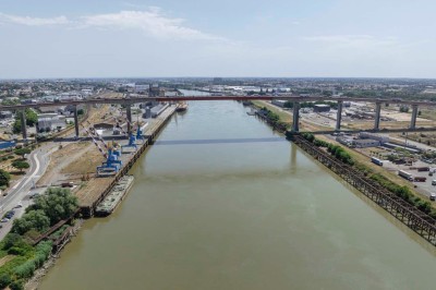 Vue aérienne d'un fleuve traversé par un pont, entouré de zones industrielles et d'infrastructures portuaires.
