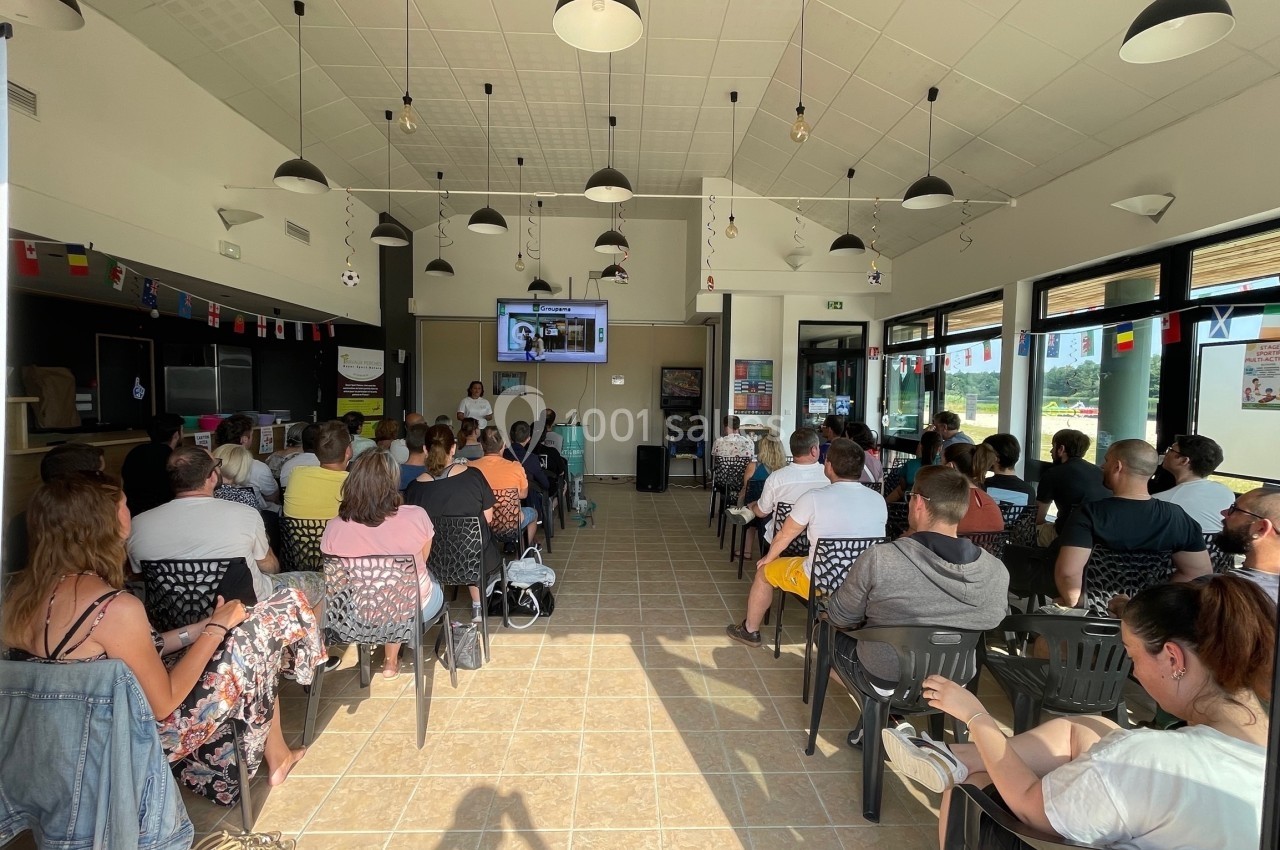 Un groupe de personnes assises dans une salle lumineuse, regardant une présentation projetée sur un écran.