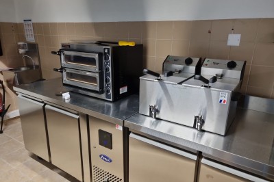 Cuisine professionnelle équipée d'un four à double étage, de deux friteuses et de plans de travail en inox.