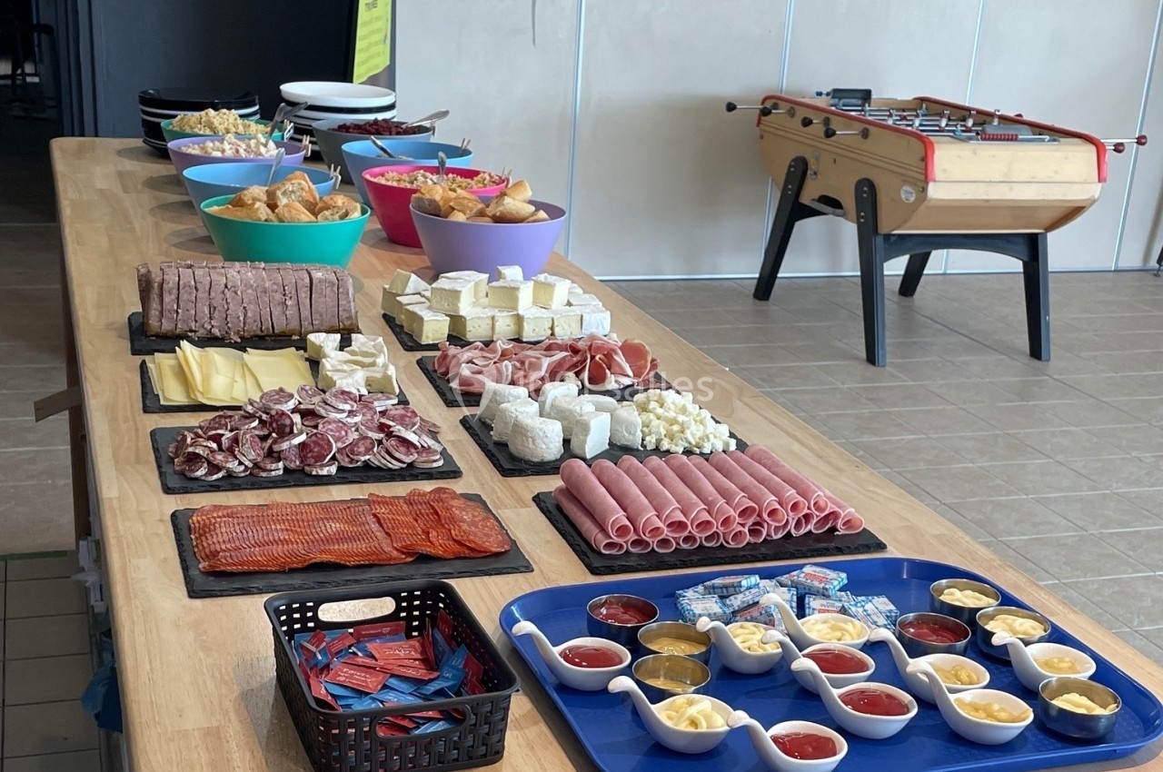 Buffet varié avec charcuterie, fromages, viennoiseries, condiments et sauces, disposé sur une longue table en bois.