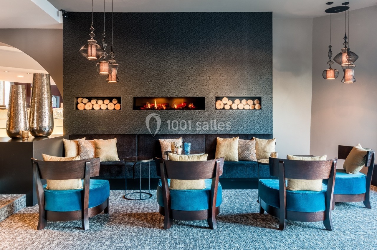 Salon moderne avec cheminée murale, fauteuils bleus, canapé noir et suspensions décoratives en métal.