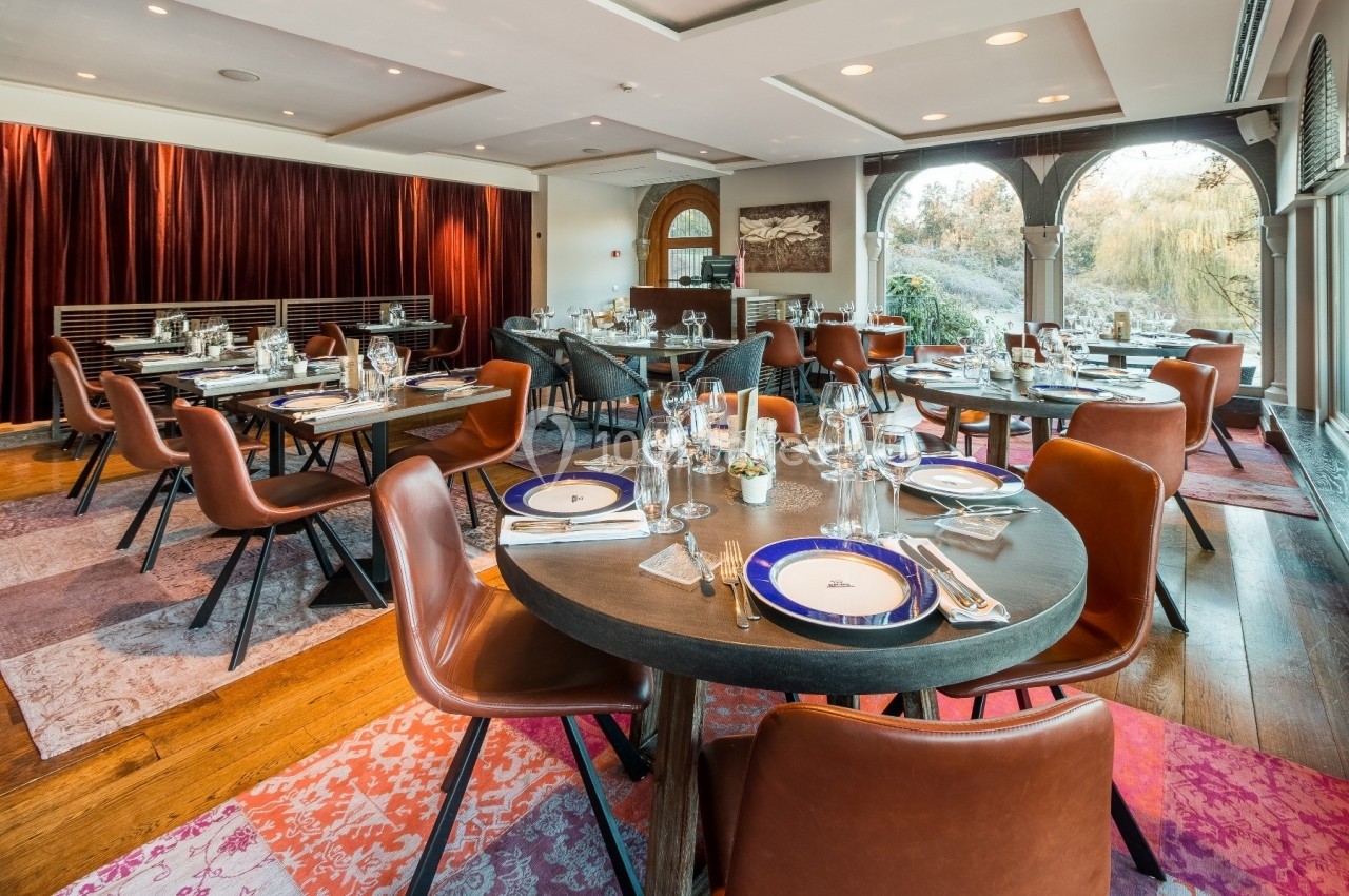 Salle de restaurant élégante avec tables dressées, chaises en cuir marron et grandes baies vitrées donnant sur un jardin.