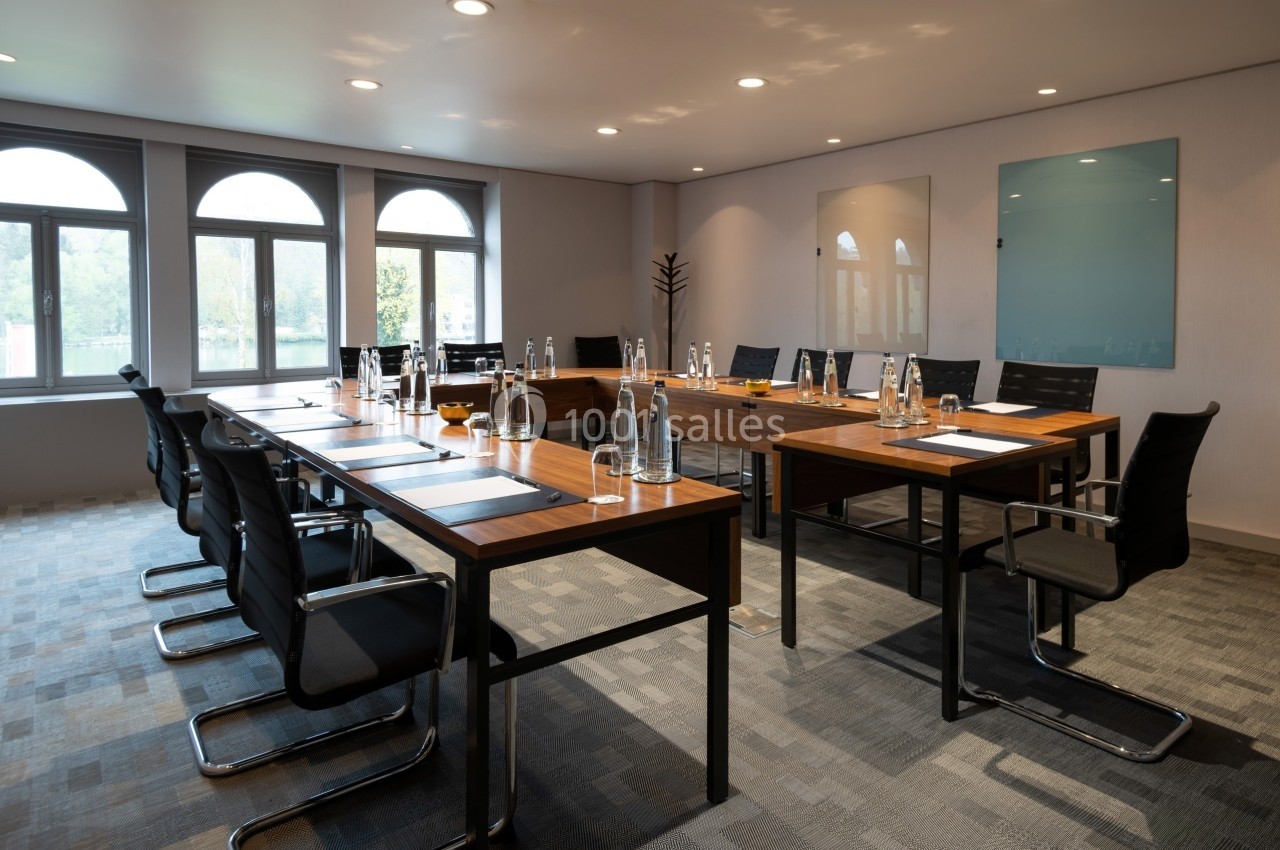 Salle de réunion lumineuse avec tables en bois, chaises noires, bouteilles d'eau et blocs-notes disposés.