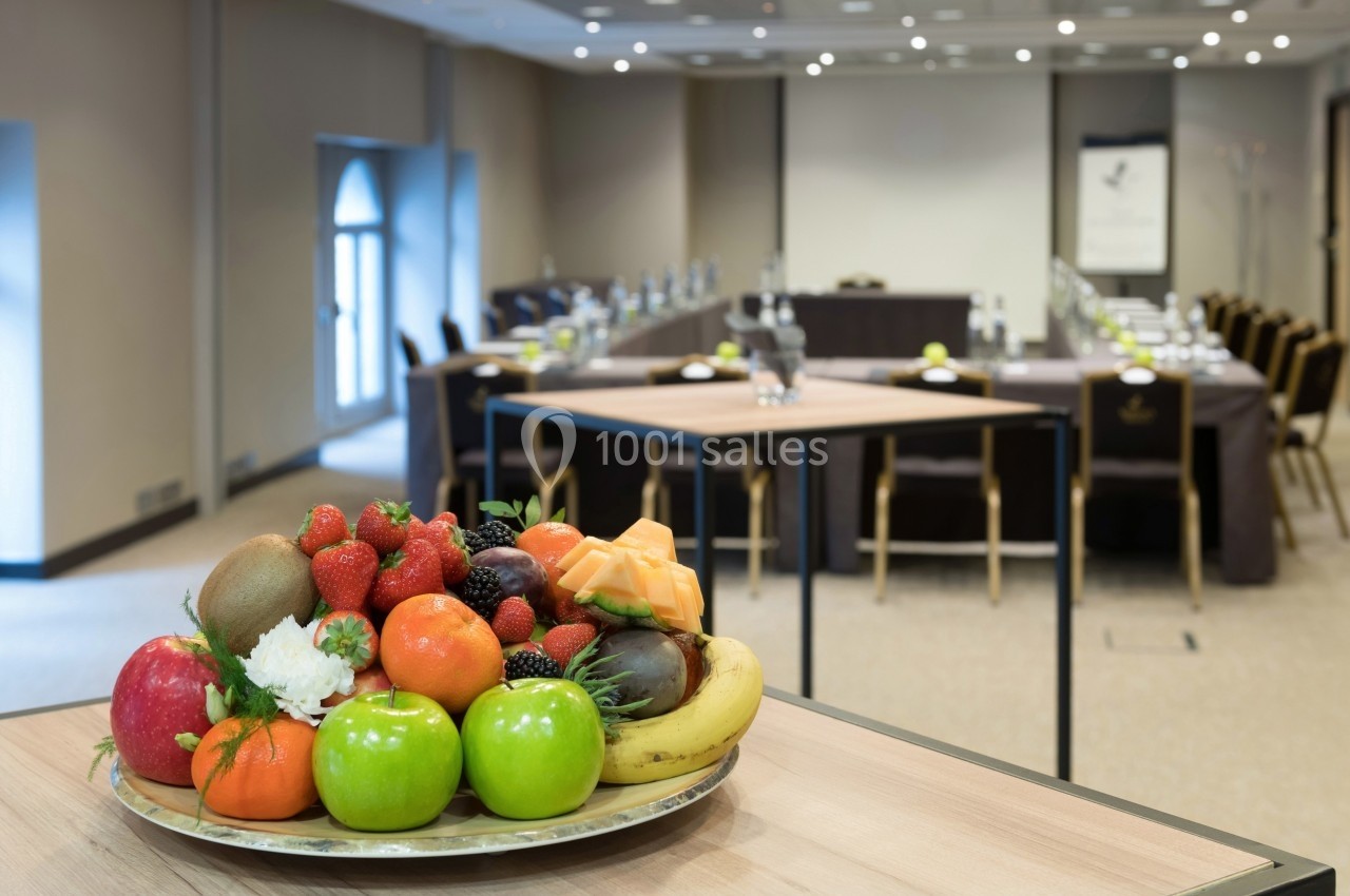 Plateau de fruits variés sur une table en premier plan, avec une salle de réunion aménagée en arrière-plan flou.