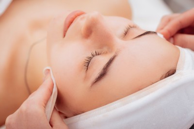 Miniature Location salle Rixensart (Brabant wallon) - Martin's Château du Lac #16 Femme allongée recevant un soin du visage avec un bandeau blanc, une personne nettoie sa peau avec des cotons.