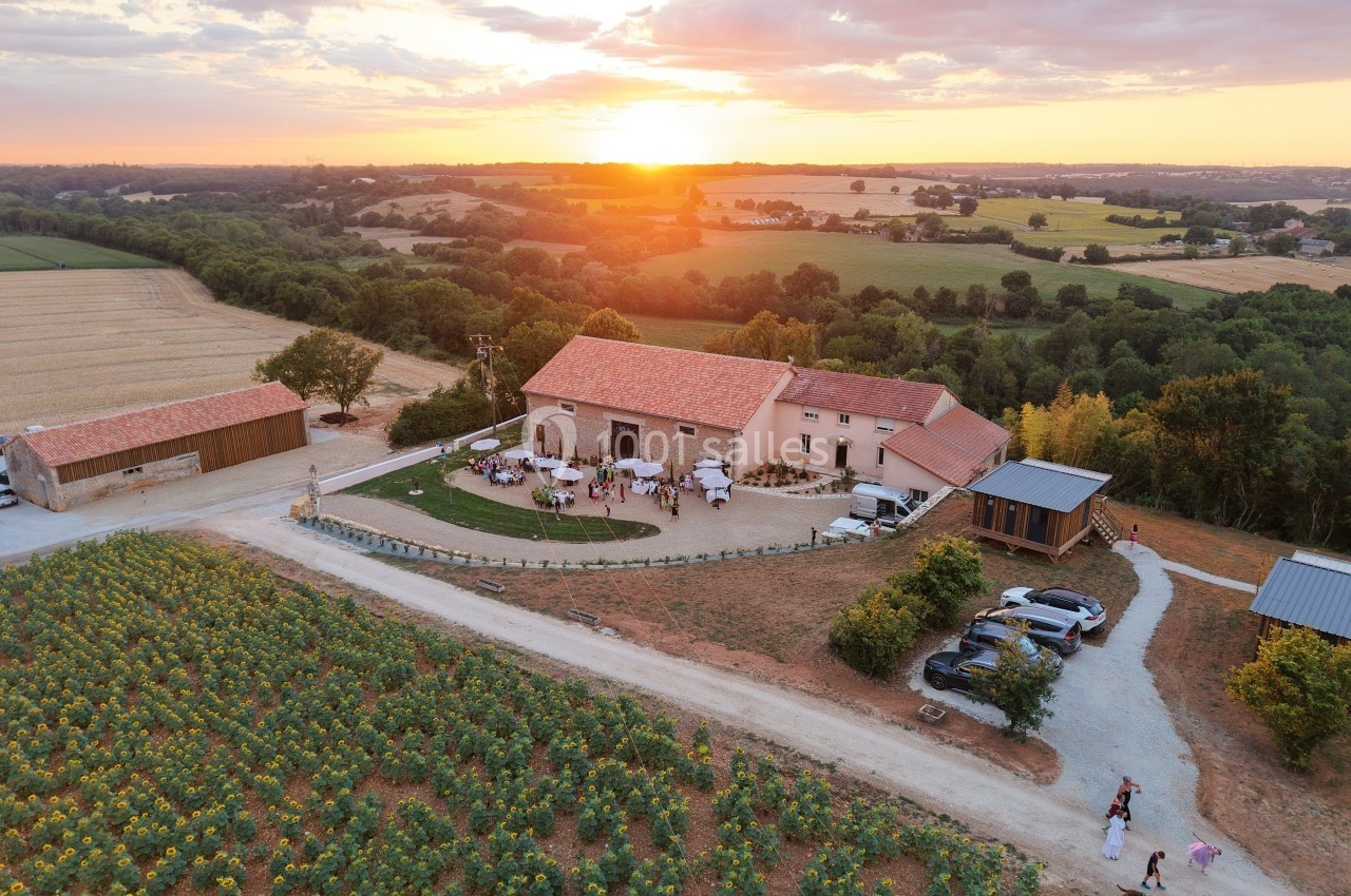 Vue aérienne d'une ferme avec des bâtiments en pierre, entourée de champs et d'arbres, au coucher du soleil.