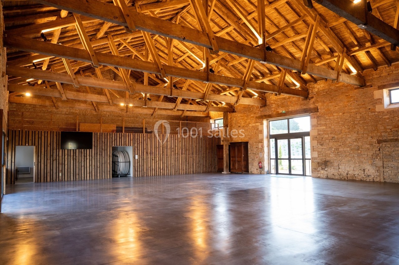 Intérieur d'une grande salle avec charpente en bois apparente, murs en pierre et sol en béton poli.