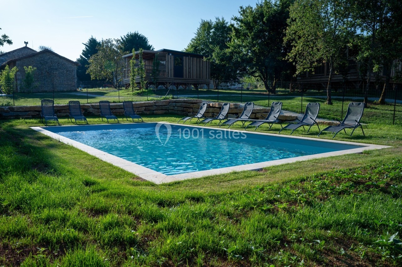 Piscine rectangulaire entourée de chaises longues sur une pelouse, avec des arbres et des bâtiments en arrière-plan.