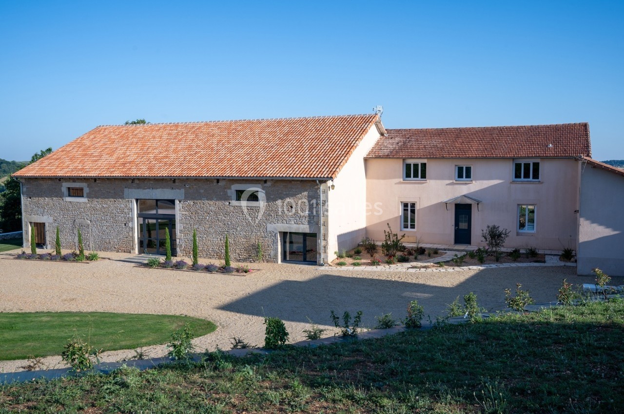 Bâtiment rénové en pierre et crépi avec toit en tuiles, entouré d'une cour gravillonnée et d'espaces verts.
