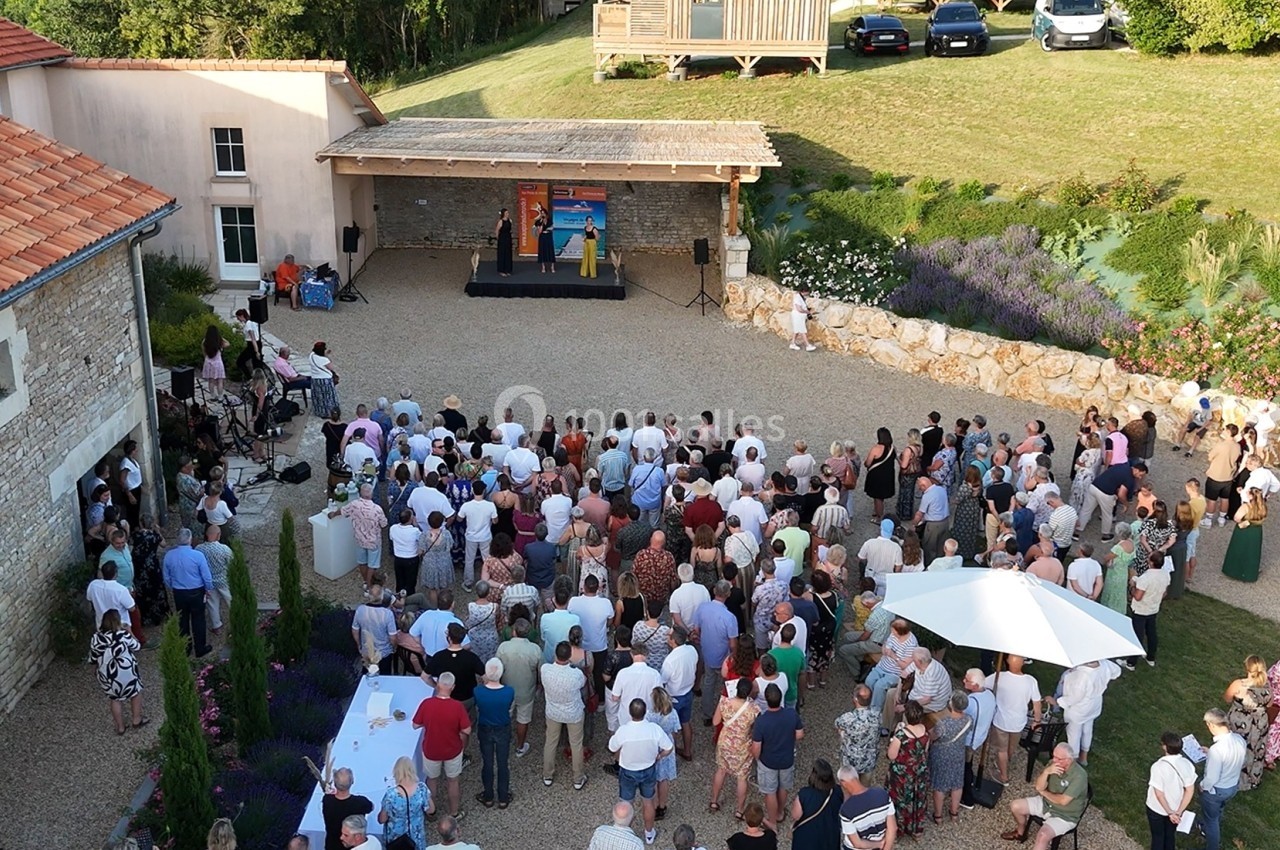 Vue aérienne d'une cérémonie en plein air avec des spectateurs rassemblés devant une scène dans une cour.