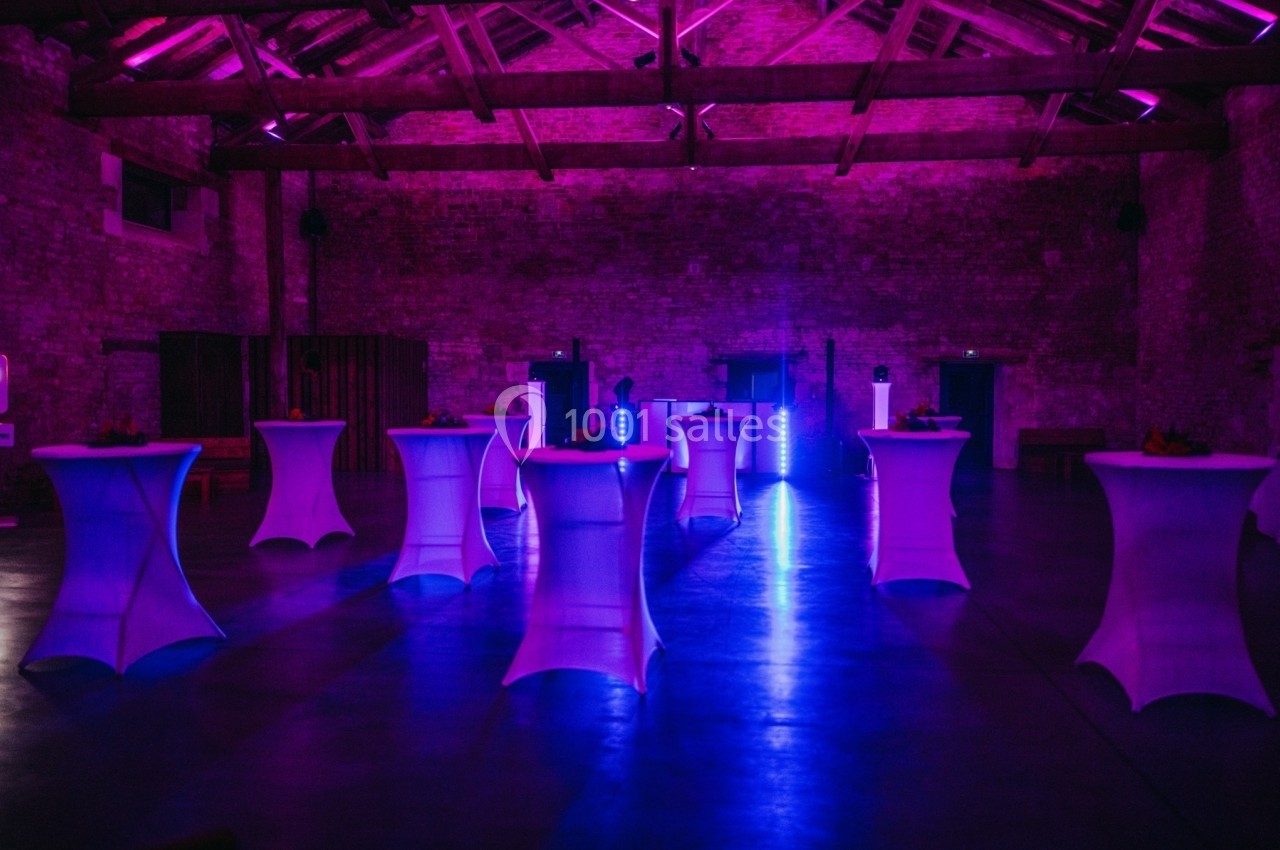 Salle en pierre avec des tables hautes éclairées par une lumière violette, ambiance de réception ou événement.