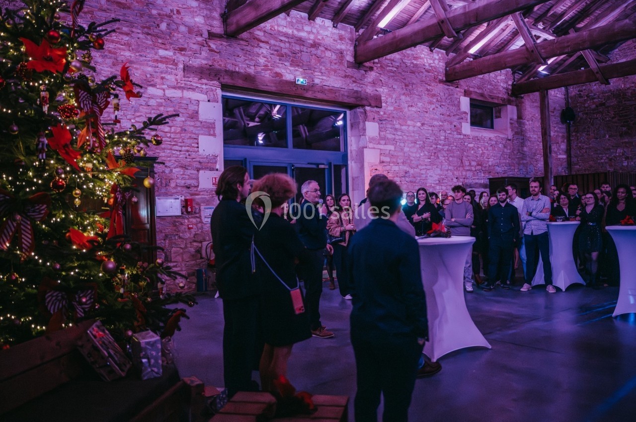 Groupe de personnes réunies dans une salle en pierre, décorée avec un sapin de Noël illuminé.