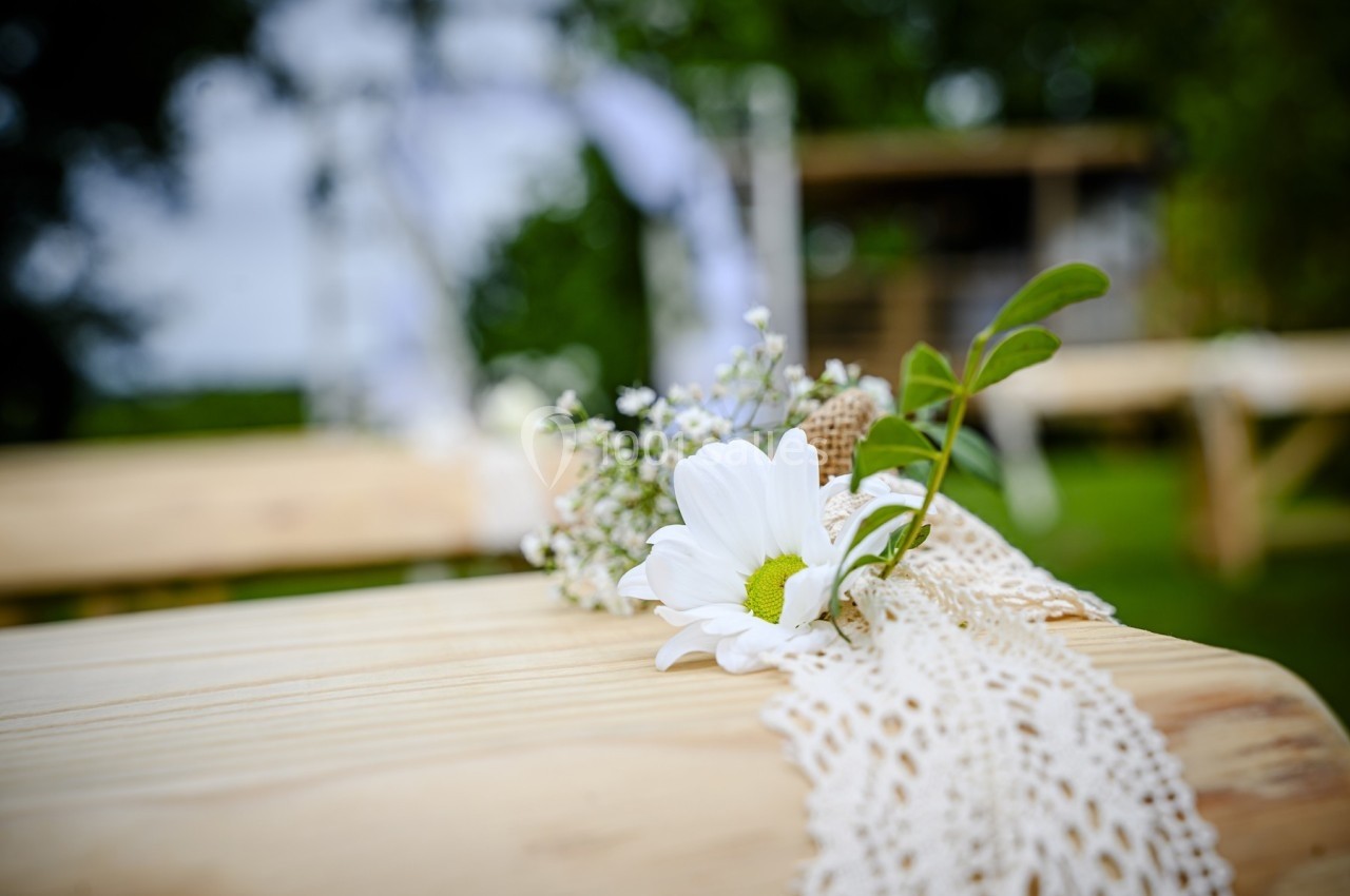 Fleur blanche et verdure posées sur une table en bois décorée de dentelle, en extérieur.