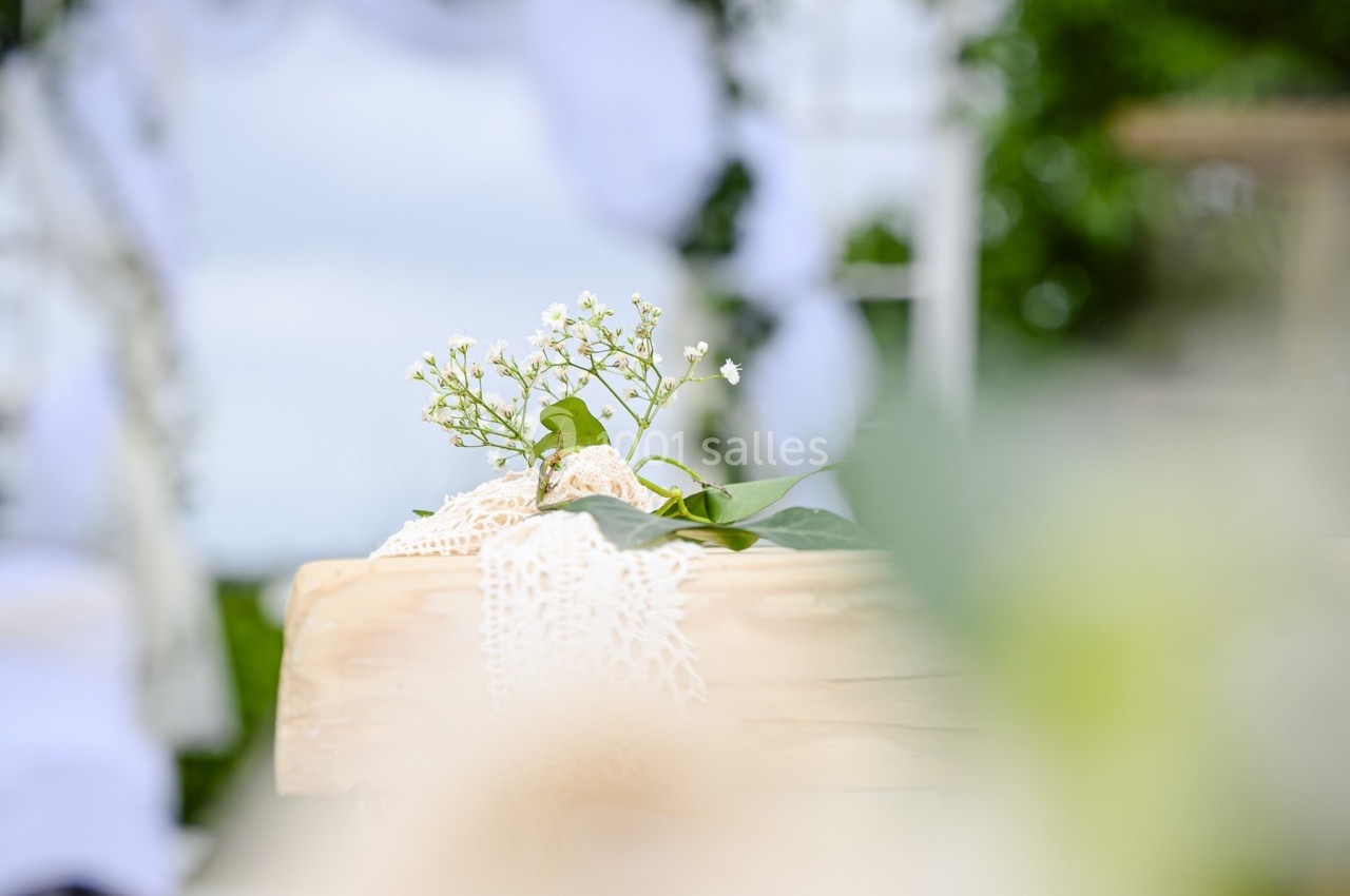 Décoration florale délicate sur une table en bois, avec un arrière-plan flou de cérémonie en extérieur.