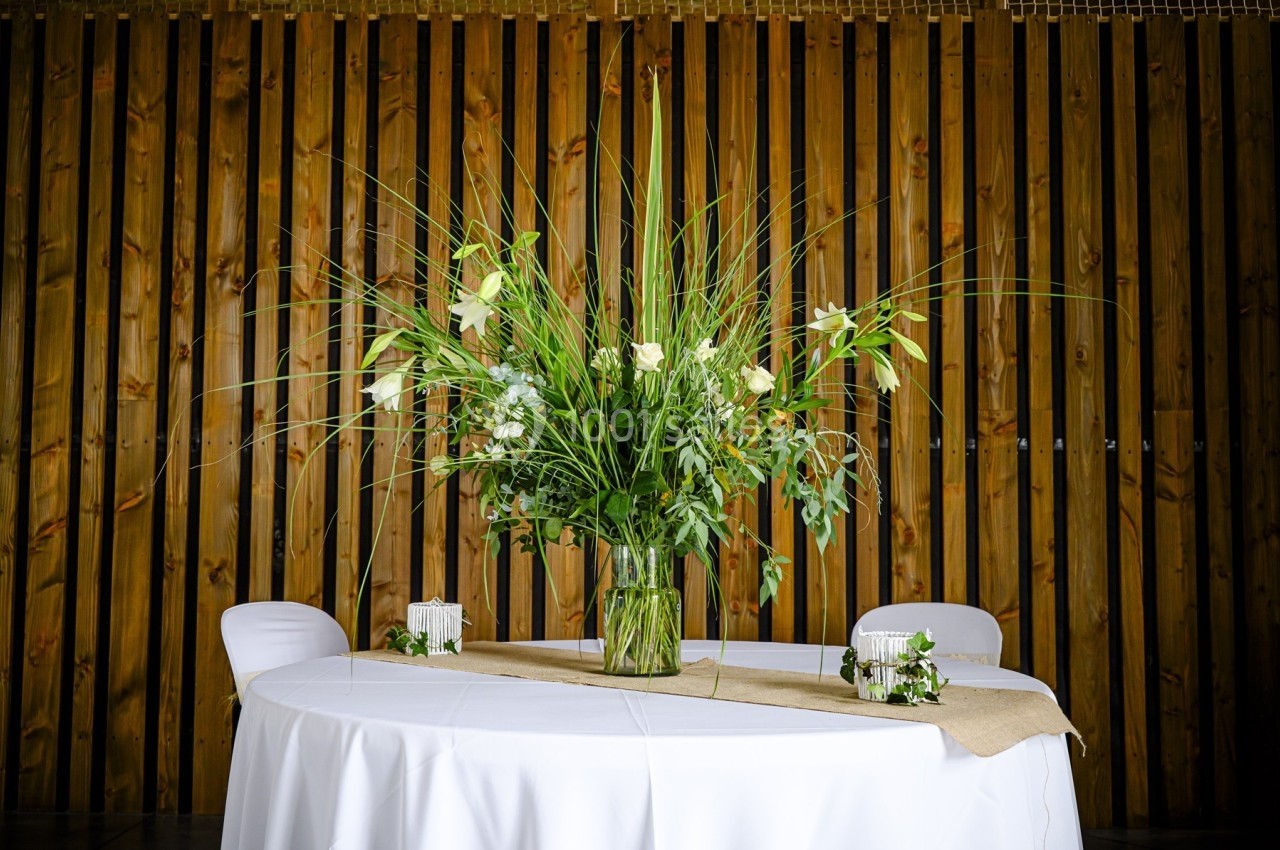 Centre de table avec un grand bouquet de fleurs blanches et feuillages verts, posé sur une table ronde blanche.