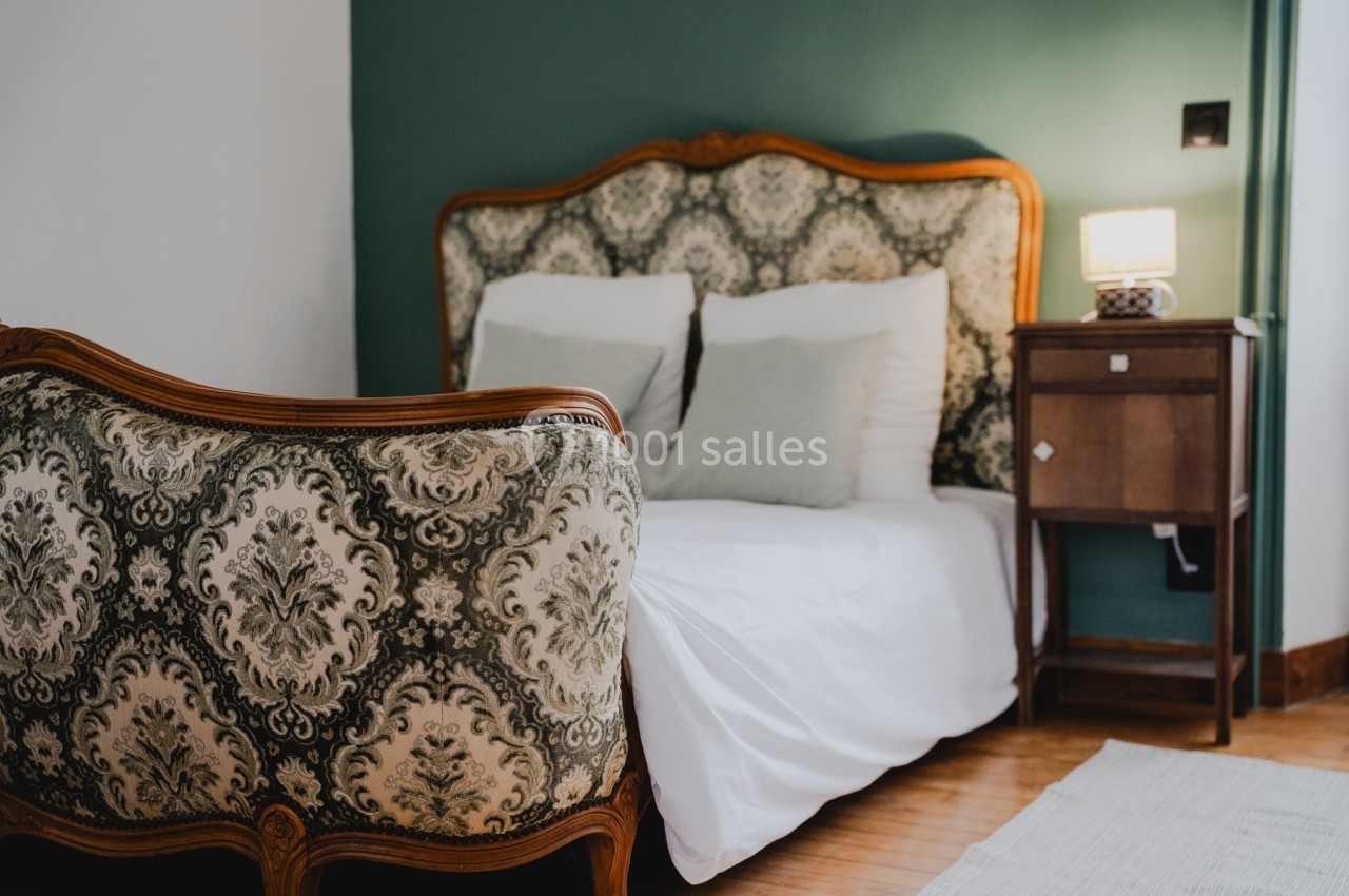 Lit avec tête de lit et fauteuil en bois sculpté, tapissés de motifs baroques, dans une chambre au mur vert.