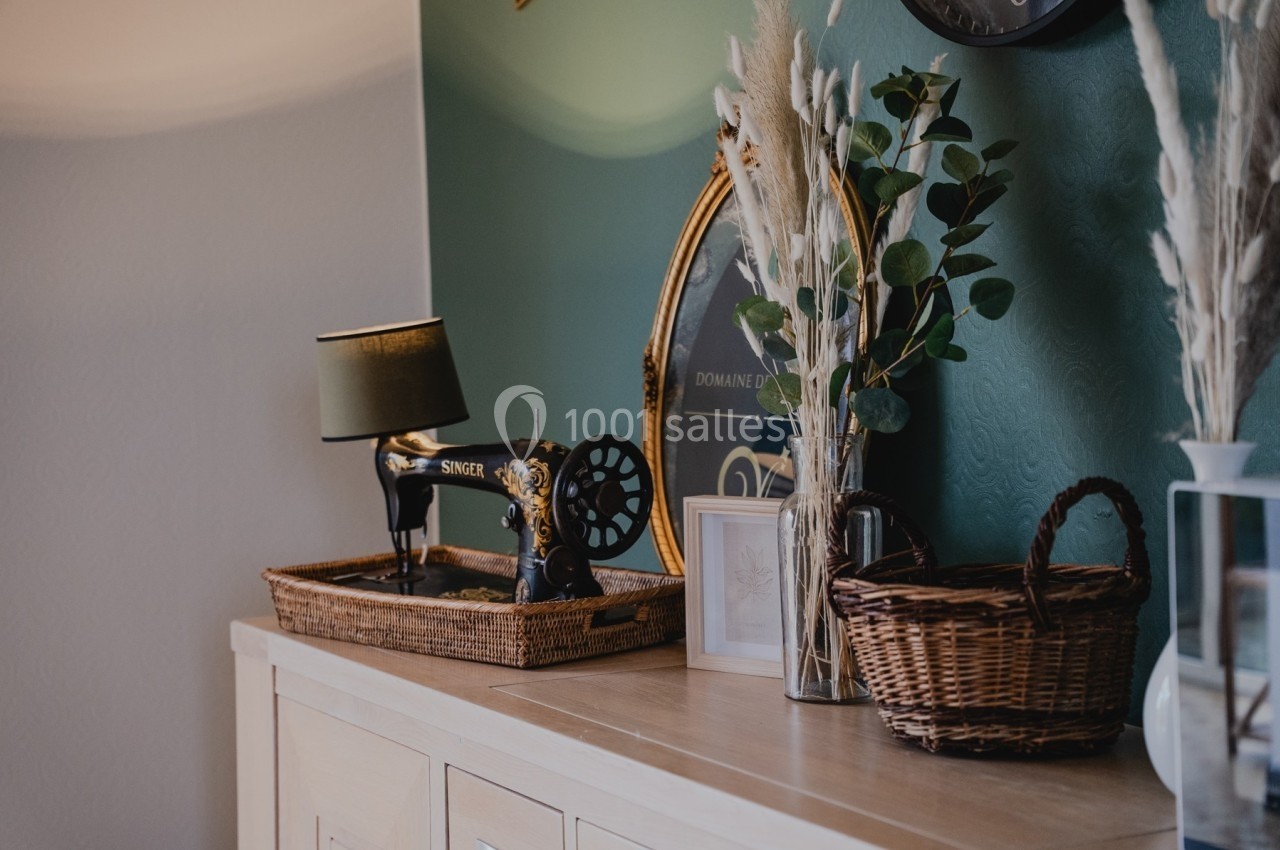 Machine à coudre vintage sur un buffet en bois, entourée de paniers en osier, plantes et décorations murales.