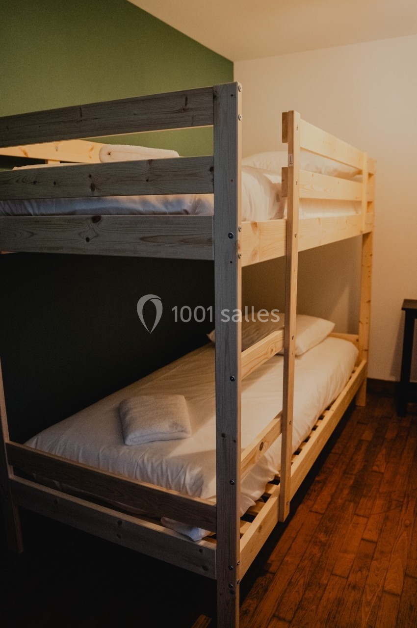 Lit superposé en bois clair avec matelas et linge de lit blanc dans une chambre à parquet et mur vert.