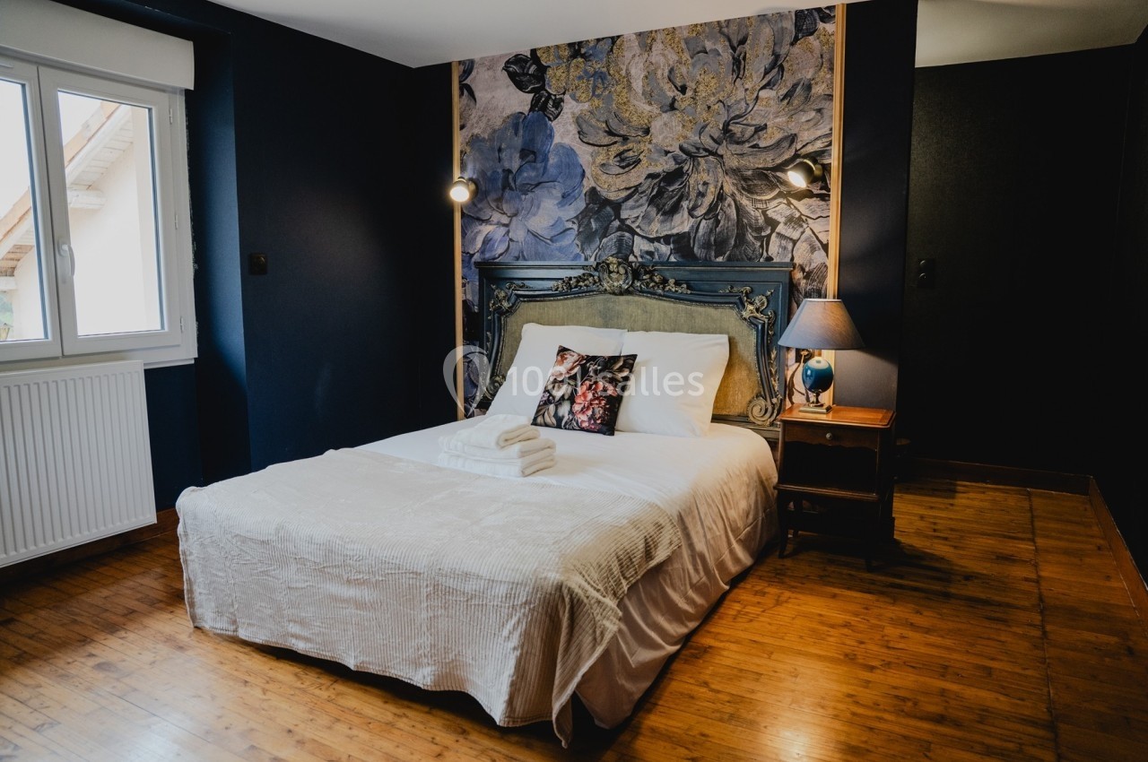 Chambre avec lit double, tête de lit décorative, mur fleuri, lampe de chevet et parquet en bois.
