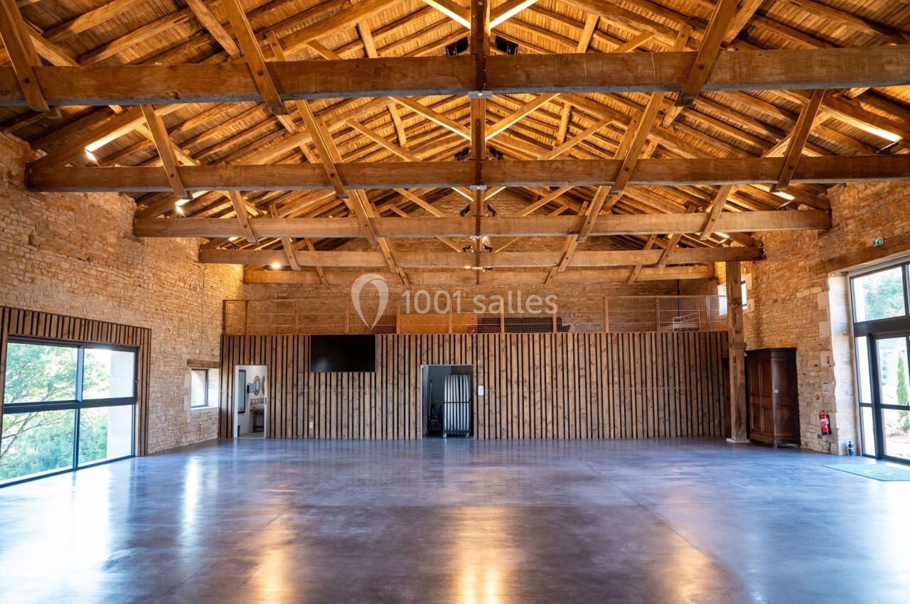 Intérieur d'une grande salle rénovée avec charpente en bois apparente, murs en pierre et sol en béton poli.