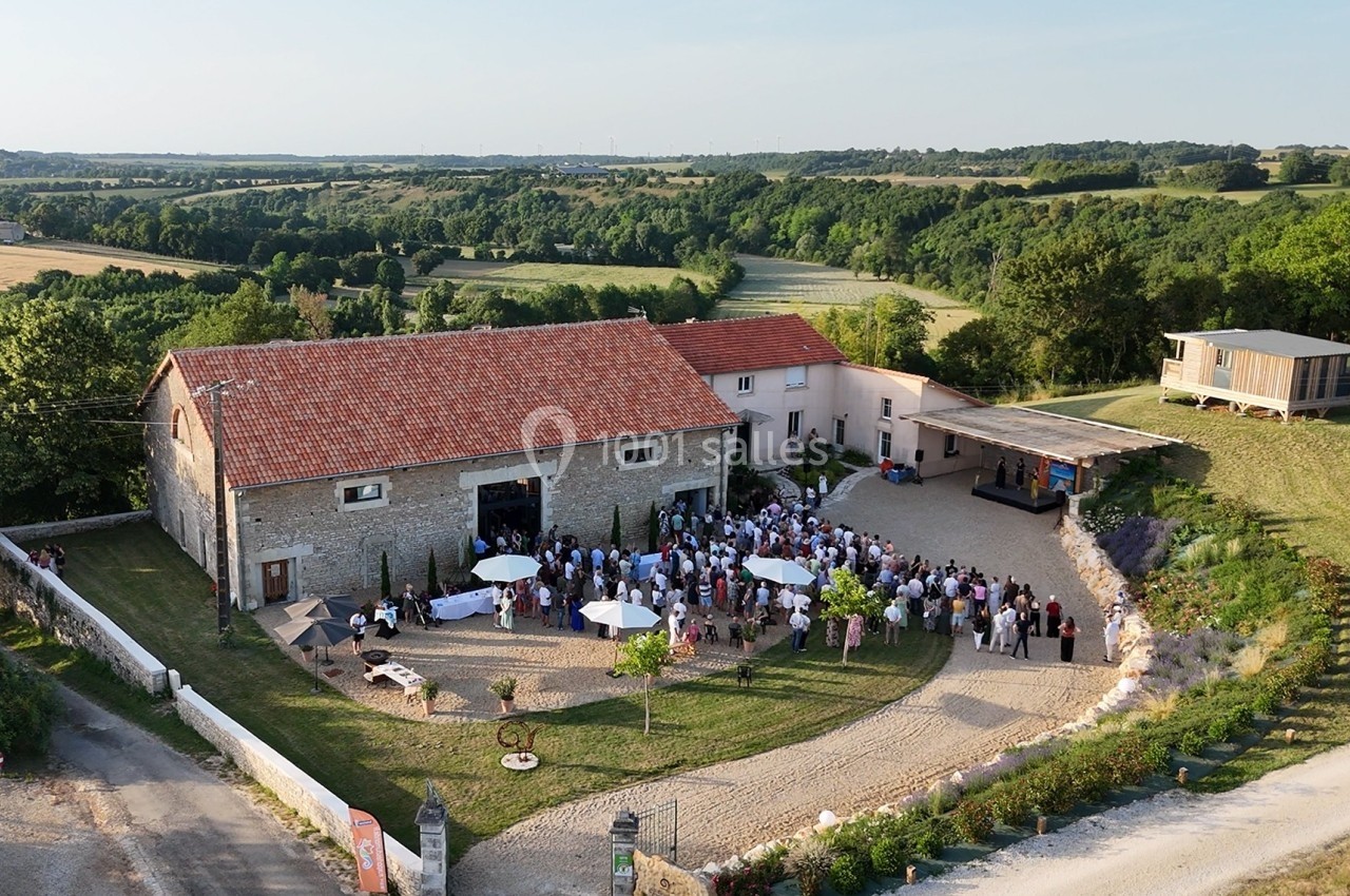 Vue aérienne d'une réception en plein air devant une grande bâtisse en pierre entourée de champs et de verdure.