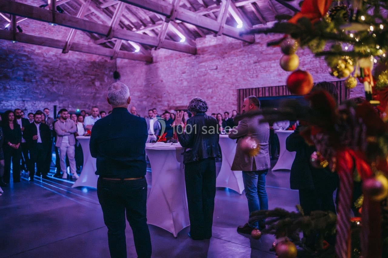 Groupe de personnes réunies dans une salle en pierre décorée pour Noël, écoutant une intervention près de tables hautes.