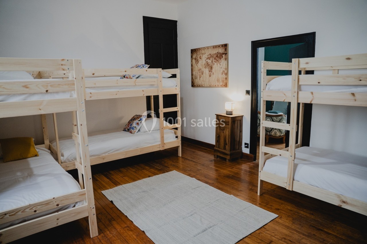 Chambre avec quatre lits superposés en bois, parquet au sol, tapis clair et une lampe posée sur un meuble en bois.