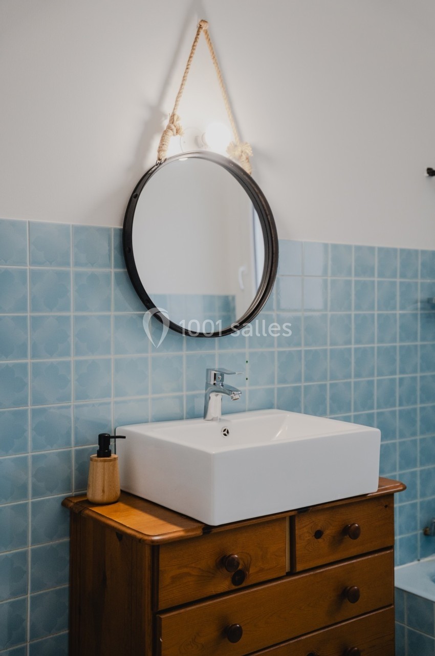 Lavabo blanc sur meuble en bois avec miroir rond suspendu, carrelage mural bleu en arrière-plan.
