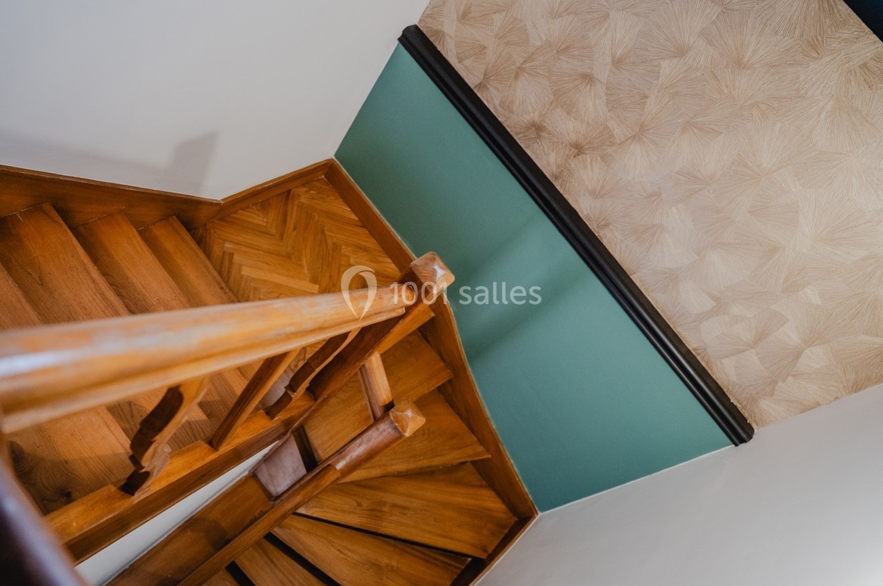 Escalier en bois avec rampe, vu de haut, menant à un mur vert et beige texturé.