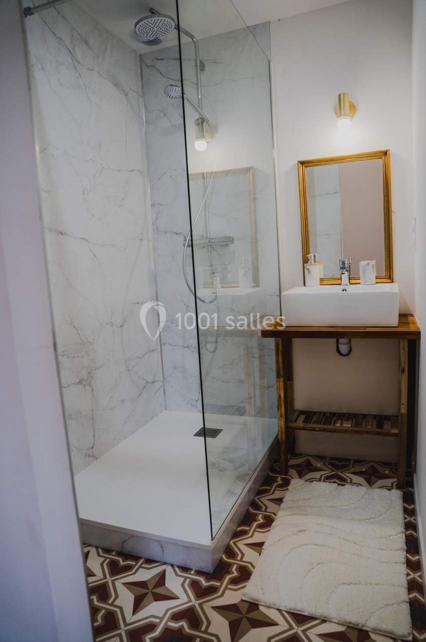 Salle de bain avec douche à l'italienne vitrée, lavabo sur meuble en bois et miroir encadré, sol en carreaux décoratifs.