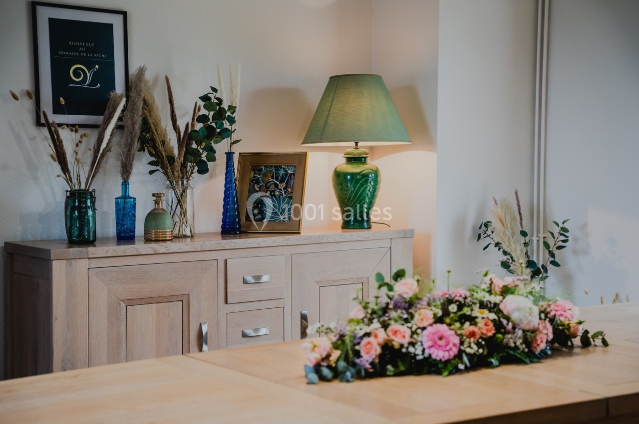 Buffet en bois décoré de vases, lampe verte et cadre, avec un bouquet de fleurs sur une table au premier plan.