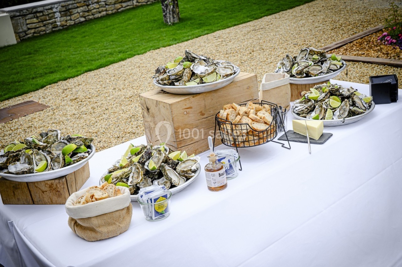 Plateau de fruits de mer avec huîtres, citrons, pain et condiments disposés sur une table blanche en extérieur.
