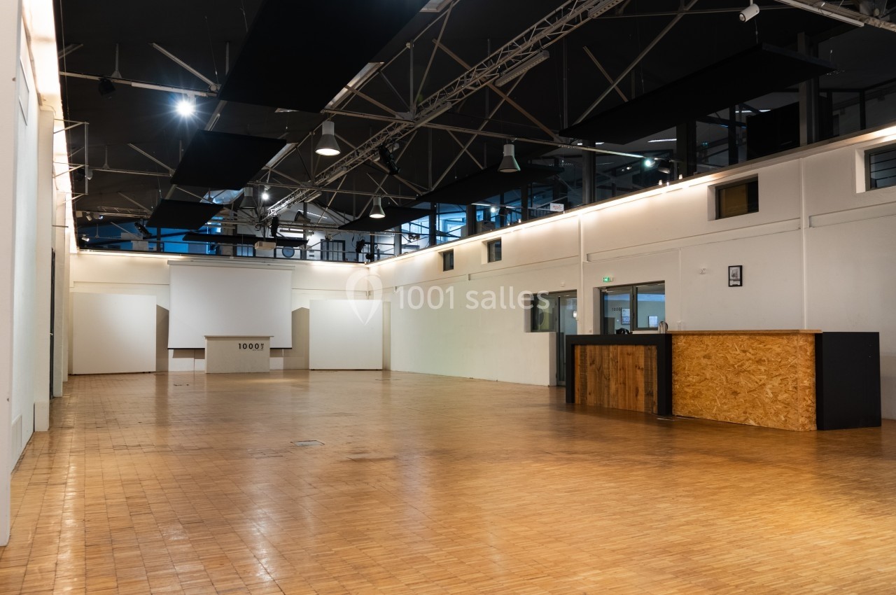 Salle spacieuse avec parquet en bois, plafond industriel et comptoir en bois à droite.