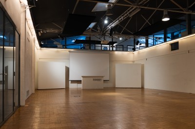 Espace intérieur lumineux avec plantes, tables et chaises, sol en béton et grandes baies vitrées.